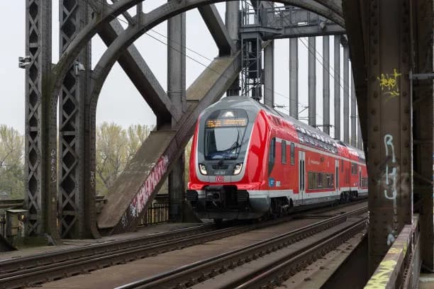 Tren regional rojo de Deutsche Bahn cruzando un puente ferroviario de estructura metálica en Frankfurt, Alemania, con arcos de acero en primer plano