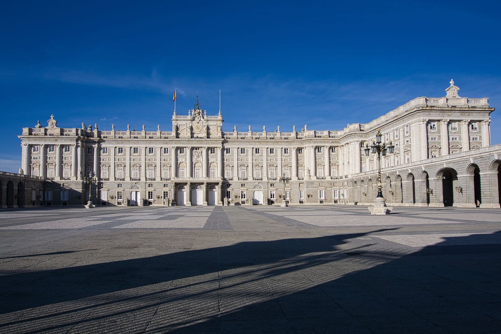 La Puerta de Alcalá de Madrid con sus arcos de piedra y parterres de flores naranjas en un día soleado